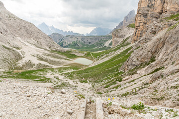 View on alpine lake in the Italian Dolomites high in the mountains on a cloudy summer day. Impressive mountains with grassy slopes. Mountains in the background. Acitve lifestyle, outdoor adventure.