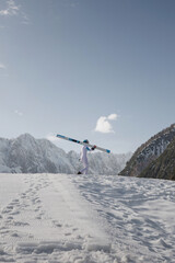 Fototapeta premium Ski jumper walking across a ski slope, with skis on his shoulder, in the beautiful winter mountain landscape. Ski sports concept.