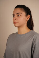 Close-up portrait of a young woman in a gray T-shirt on a light background. The natural look emphasizes the young age of the girl. The picture shows a woman with dark hair.
