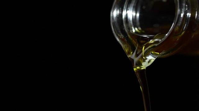 Extra virgin olive oil being poured out a clear glass bottle on a black background, close up, slow motion . Organic liquid flowing, copy space