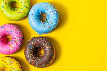 Colorful donuts on yellow background. Top view with copy space.
