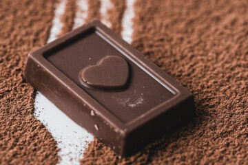 Slice of chocolate bar with heart on background cocoa powder.