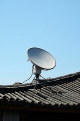 Satellite dish atop weathered tiled roof, clear sky.