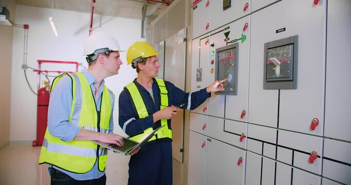 Engineers Collaborating in Industrial Control Room electrical control panel with Safety Gear and Equipment, Monitoring Systems, and Discussing Technical Operations for Efficient Facility Management