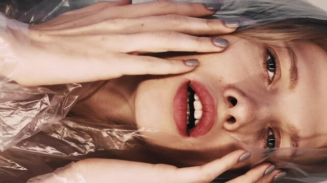 Vertical video. Anxiety attack. Mental disorder. Defocused art portrait of disturbed beautiful woman in polyethylene film hood suffering from pain fainting on beige.