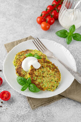 Zucchini fritters or zucchini pancakes on a white plate with fresh basil and sour cream. Top view, selective focus.