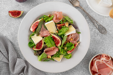 Fresh salad with figs, prosciutto or jamon, brie cheese and walnuts on a concrete background.