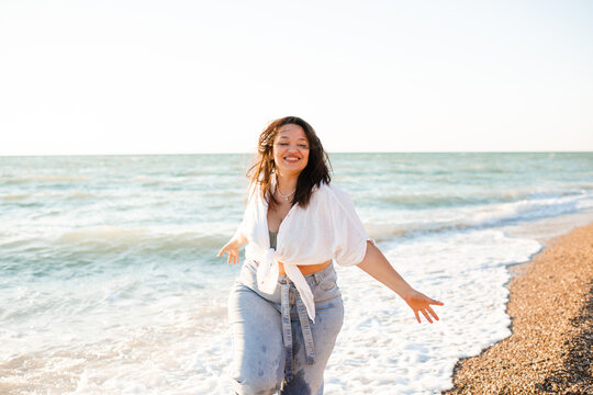 Happy young adult woman 30-35 year old having fun over sea at beach outdoor. Summer time. Vacation season.