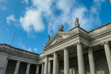 Fototapeta premium Classical building with tall columns and triangular pediment stands against blue sky. Grand architecture suggest a public building, likely the Bank of Ireland (formerly the Irish Parliament) in Dublin