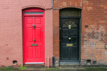 Two adjacent front doors of terraced houses in Dublin, Ireland. One door is bright red, and the other is black. Both have distinctive lion head door knockers. Houses are built of brick. Residential