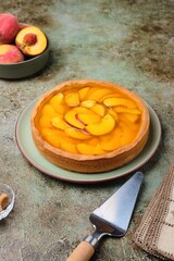 Summer pie on shortcrust pastry with custard, fresh peach slices and jelly on a green ceramic plate on a green concrete background.