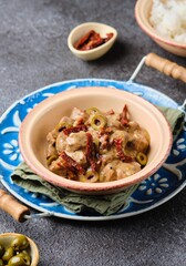 A hot dish, stewed beef with dried tomatoes and olives in a clay bowl on a blue meallic tray on a dark concrete background. Beef recipes.