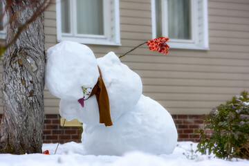 A large snowman melted and buried his head in a tree. A drunk snowman in the yard of a house.