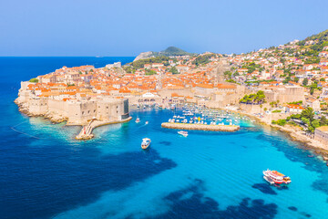 A vivid drone photograph of Dubrovnik's Old Town featuring ancient walls, red rooftops, and historic architecture, all surrounded by the sparkling Adriatic Sea and enhanced with vibrant summer tones.