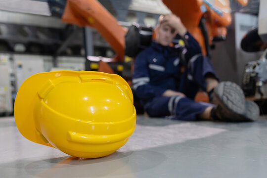 Close-up on yellow hard hat with blurred injured factory worker on the floor as a background