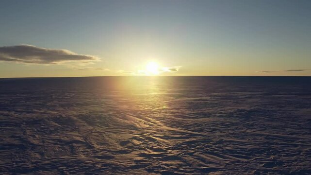 Amazing sunset in Antarctica. Endless snow landscape. Earth ecology protection. Global warming and ice melting. Drone camera is rising up in front of the sun.