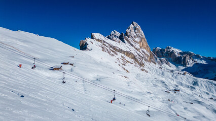 Seceda on the Val Gardena resort presents an awe-inspiring winter spectacle, captured from the air by drone. Its iconic jagged peaks rise dramatically above snow-covered slopes