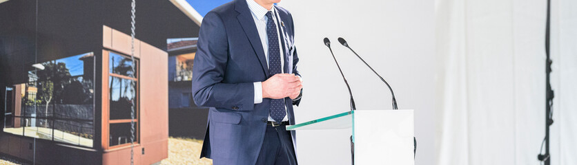 unrecognizable businessman in blue suit speaks into microphones at event