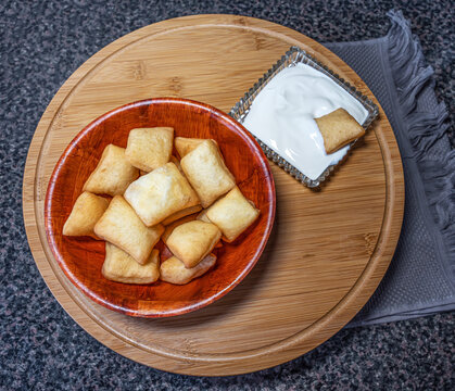 Top view of a table served with traditional dishes of the peoples of Central Asia - boorsok (baursak) and kaymak (sour cream), located on a round wooden board.