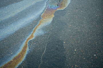 Obraz premium Colorful oil slick spreads across pavement in urban setting during daylight hours