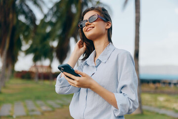 Sunglasseswearing woman checks her phone while standing in a park, surrounded by palm trees
