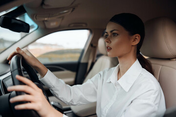 Woman, car, driver a woman in a white shirt sits confidently in the driver's seat of a car, hands firmly on the steering wheel, with an engaging look directed at the camera, emphasizing driving