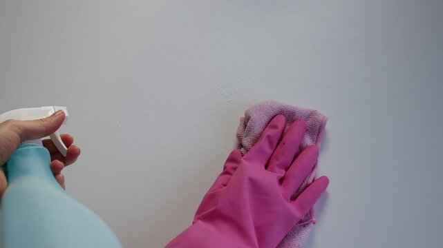 Female hands wipe white surface with pink cloth and spray. Cleaning close-up