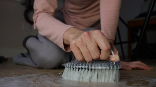 White European woman washing wooden floor with brush. House cleaning. Close-up