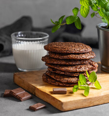 Stack of chocolate cookies on a wooden board on a dark background with a glass of milk close up.