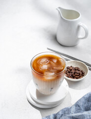 Iced coffee latte in a glass with milk on a light background with coffee beans