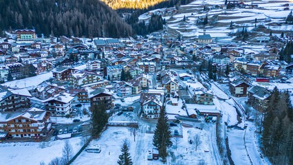 Campitello di Fassa in winter transforms into a magical alpine retreat, nestled in the heart of the Dolomites. Snow-covered peaks, charming village architecture captured by drone