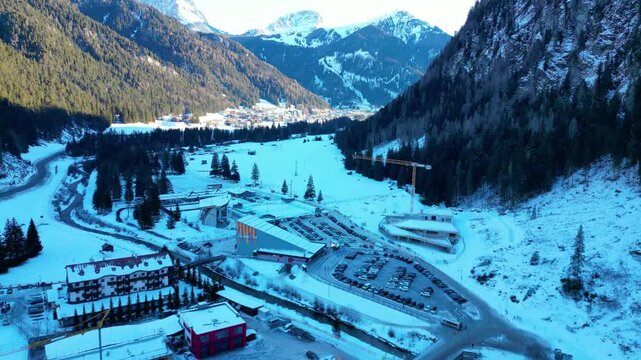 Campitello di Fassa in winter transforms into a magical alpine retreat, nestled in the heart of the Dolomites. Snow-covered peaks, charming village architecture captured by drone