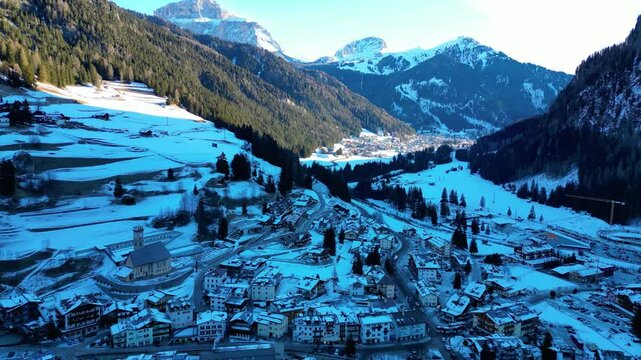 Campitello di Fassa in winter transforms into a magical alpine retreat, nestled in the heart of the Dolomites. Snow-covered peaks, charming village architecture captured by drone