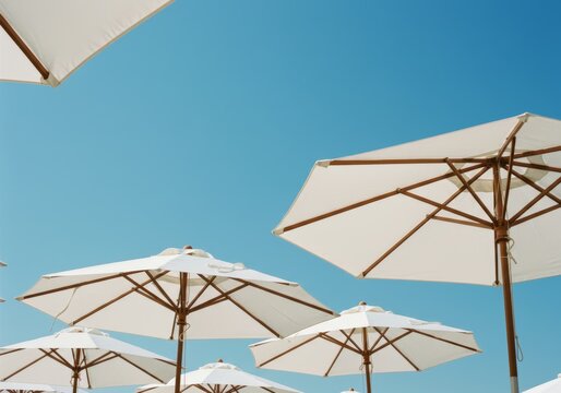 Several white beach umbrellas against a clear blue sky, creating a serene and summery atmosphere.

