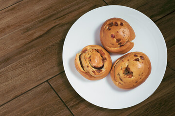 Three freshly baked rolls served on a white plate over a wooden surface