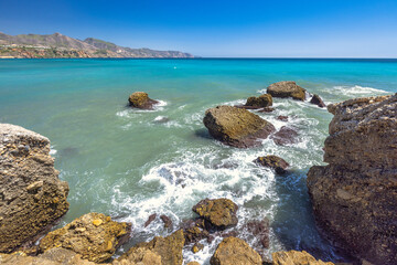 Nerja town, a resort of The Costa del Sol seaside region in Andalusia in the south of Spain, view from the Balcon de Europa square. Rocky coast meets turquoise sea under a vibrant blue sky.