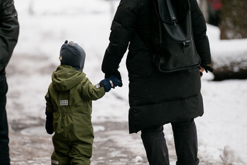 Family wearing winter coats in snow and ice filled city center. Moms holding baby boys hand in winter going to kindergarten