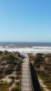 DRONE FOOTAGE - Sea, beach boulders, pebble shore and waves. Sea waves breaking on rocks. Sunny beach with sand dunes and blue sky in Esposende, Portugal. Autumn Wind Day.