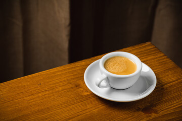 White cup of coffee on wooden table in the morning