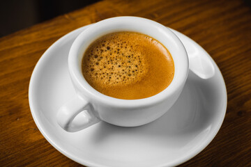 White cup of coffee on wooden table in the morning