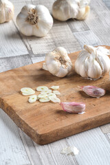 Fresh organic garlic bulbs and sliced clove on wooden cutting board. Selective focus