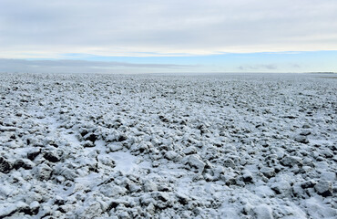 A field of black soil plowed for the winter, covered with snow against the background of a blue...