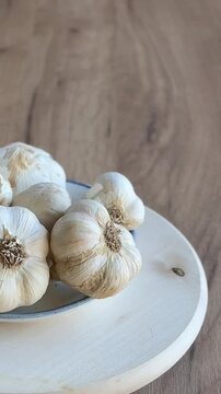 Bowl of fresh organic garlic bulbs and cloves spinning on wooden cutting board. Close up. 