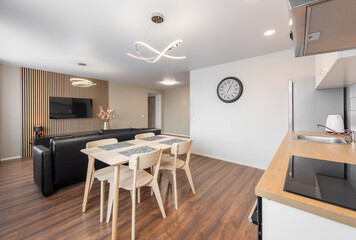 Modern Home Living Room and Kitchen Interior. Luxurious Stylish Modern Apartment. Open Space, Stylish Black Leather Sofa, White Furniture, Scandinavian Design. Cllock on the Wall, TV Screen