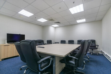 A meeting room in a modern office with a large table, comfortable chairs, a TV and a carpeted floor.