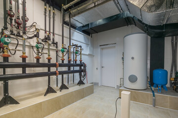 A gas boiler room with complex piping, pressure sensors, switches and a large water tank.