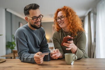 smiling couple use cellphone and credit card shopping online at kitchen