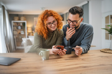 smiling couple use cellphone and credit card shopping online at kitchen