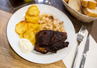 Appetizing pork cheeks baked with potatoes and beans served on platter