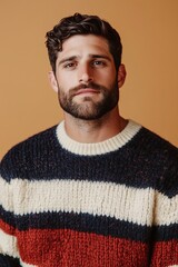 Fototapeta premium studio portrait of a man wearing a cozy striped sweater in shades of navy, cream, and red, standing in front of a warm amber background